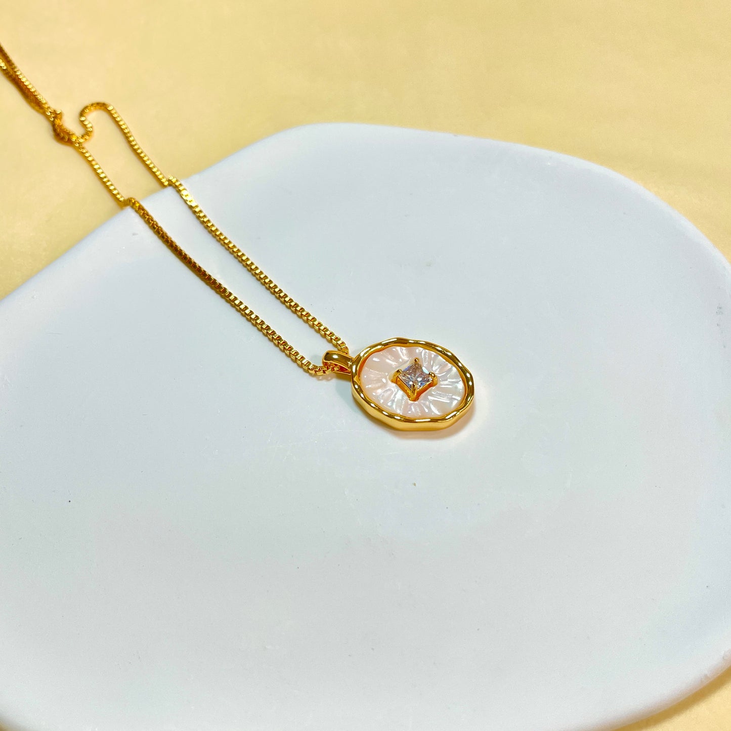 Sparkling white mother-of-pearl necklace with a central cubic zirconia on a white plate.